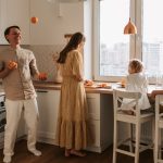 Family enjoying a playful morning in a sunlit modern kitchen with city view.