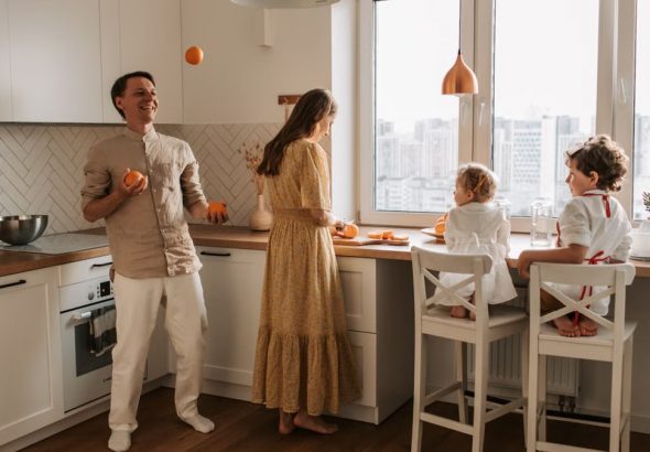 Family enjoying a playful morning in a sunlit modern kitchen with city view.